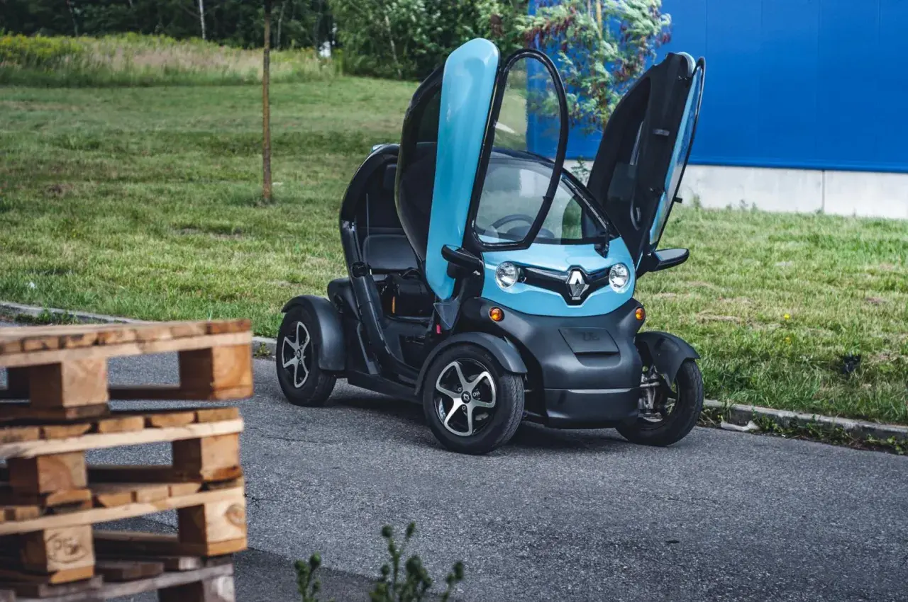 Niebiesko-czarny Renault Twizy z otwartymi drzwiami, obok drewnianych palet. Sprawdź, jaka jest renault twizy cena!