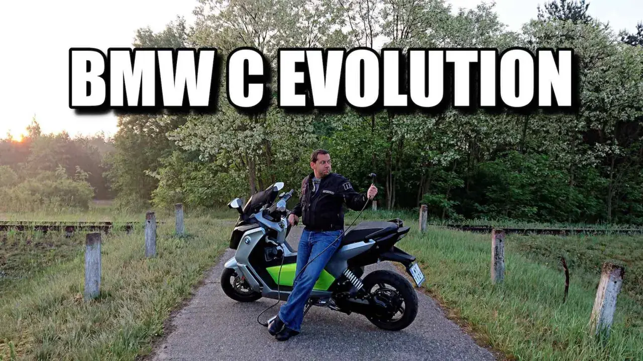 Mężczyzna siedzi na skuterze BMW C Evolution, podłączonym do ładowania. Tło to malowniczy krajobraz z drzewami.