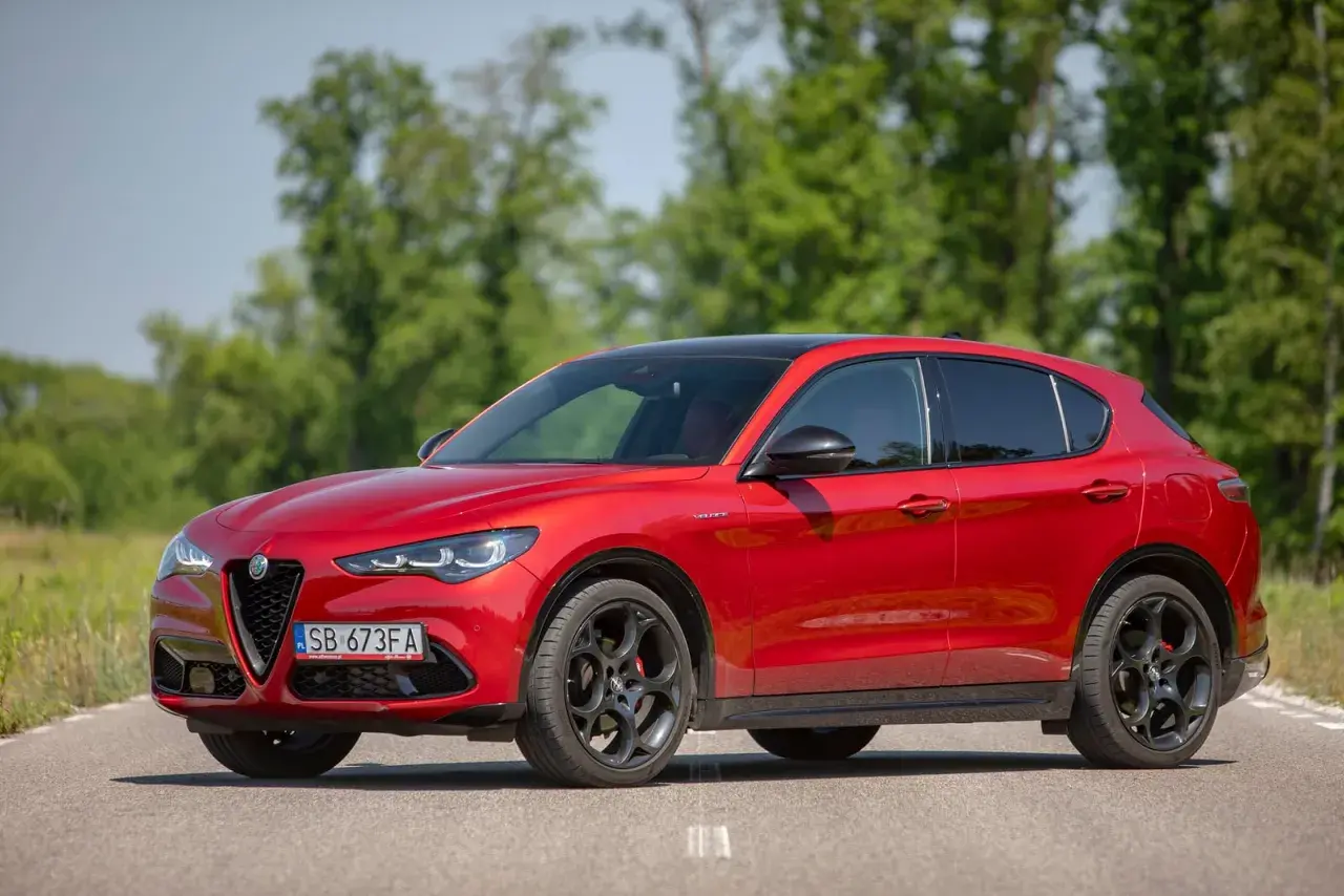 Czerwone Alfa Romeo Stelvio na drodze, z zielenią w tle. Zastanawiasz się nad jego spalaniem?