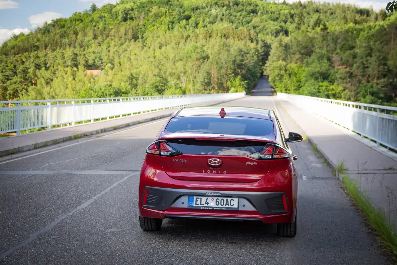 Czerwony Hyundai Ioniq Hybrid na moście, otoczony zielonymi wzgórzami.