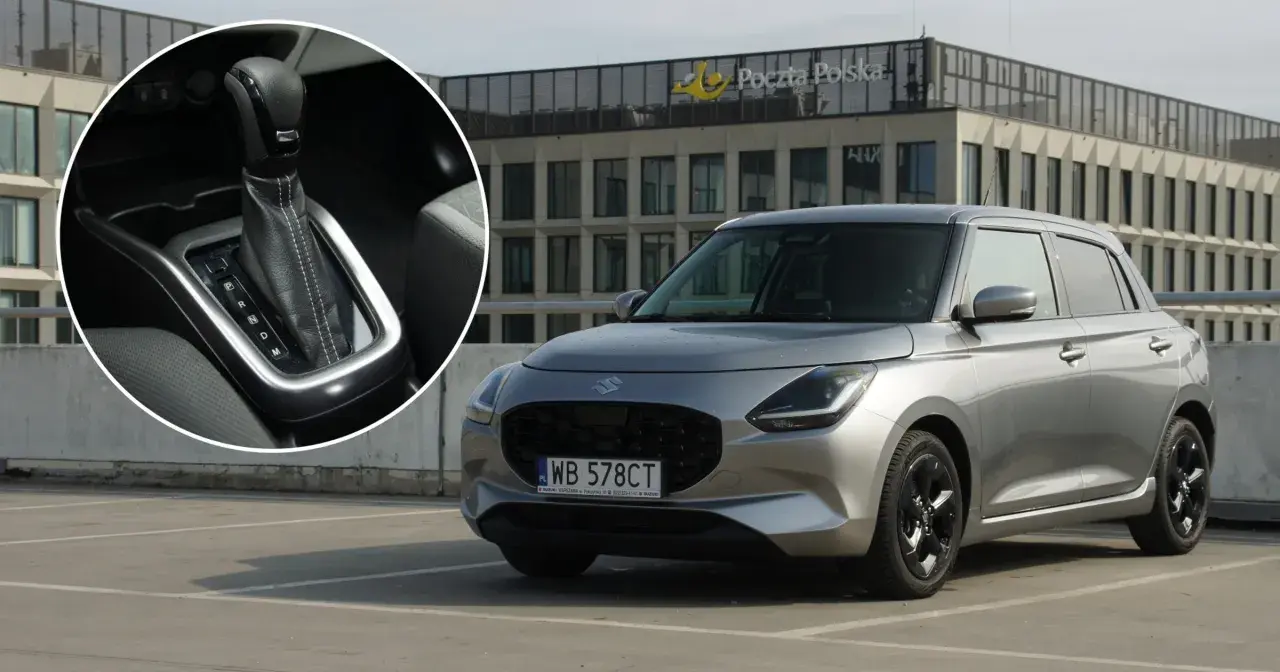 Srebrny Suzuki Swift Hybrid na parkingu przed budynkiem Poczty Polskiej. Widoczny detal dźwigni zmiany biegów.