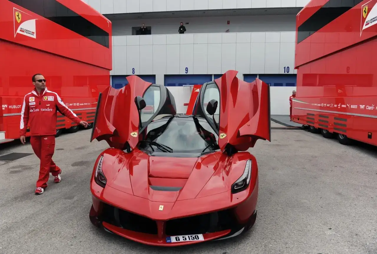 Czerwony LaFerrari z otwartymi drzwiami, obok mężczyzna w stroju Ferrari. Cena tego cacka jest astronomiczna.