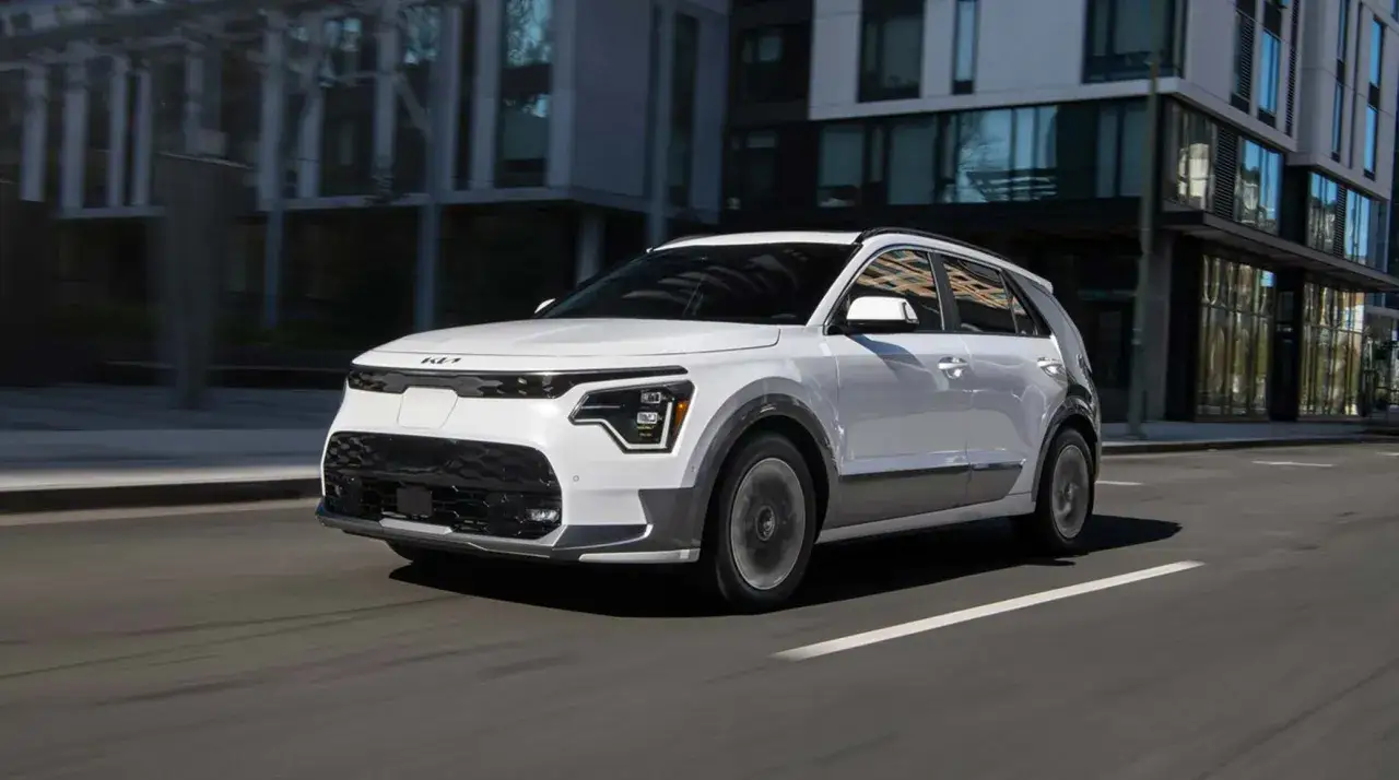 Biały Kia e-Niro jedzie ulicą miasta, otoczony nowoczesną architekturą.