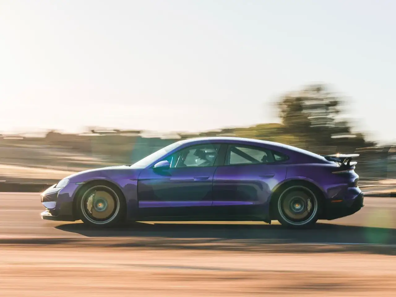 Fioletowy Porsche Taycan Turbo pędzi po torze, jego sylwetka rozmyta przez prędkość.