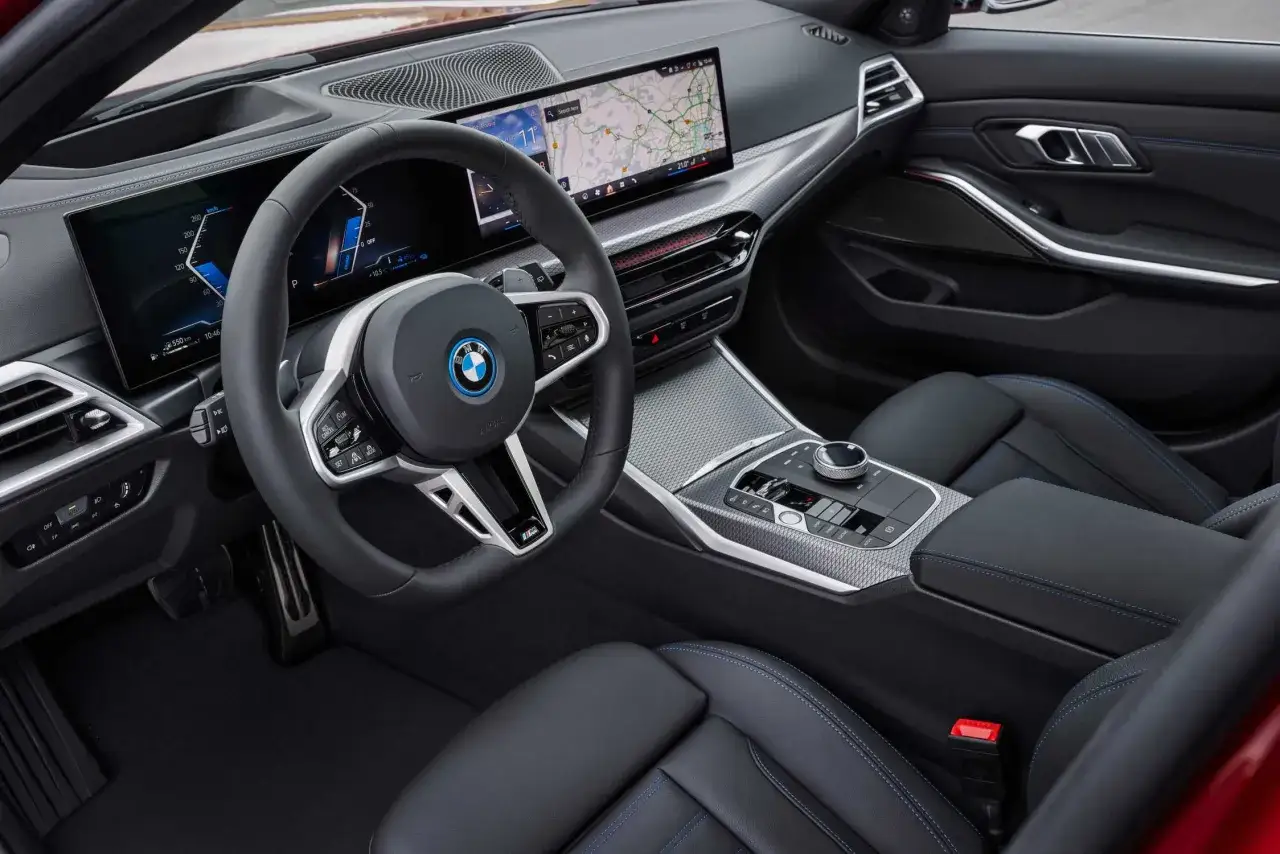 Wnętrze BMW 330e: cyfrowe zegary, ekran nawigacji, kierownica M, czarna skóra z niebieskimi przeszyciami.