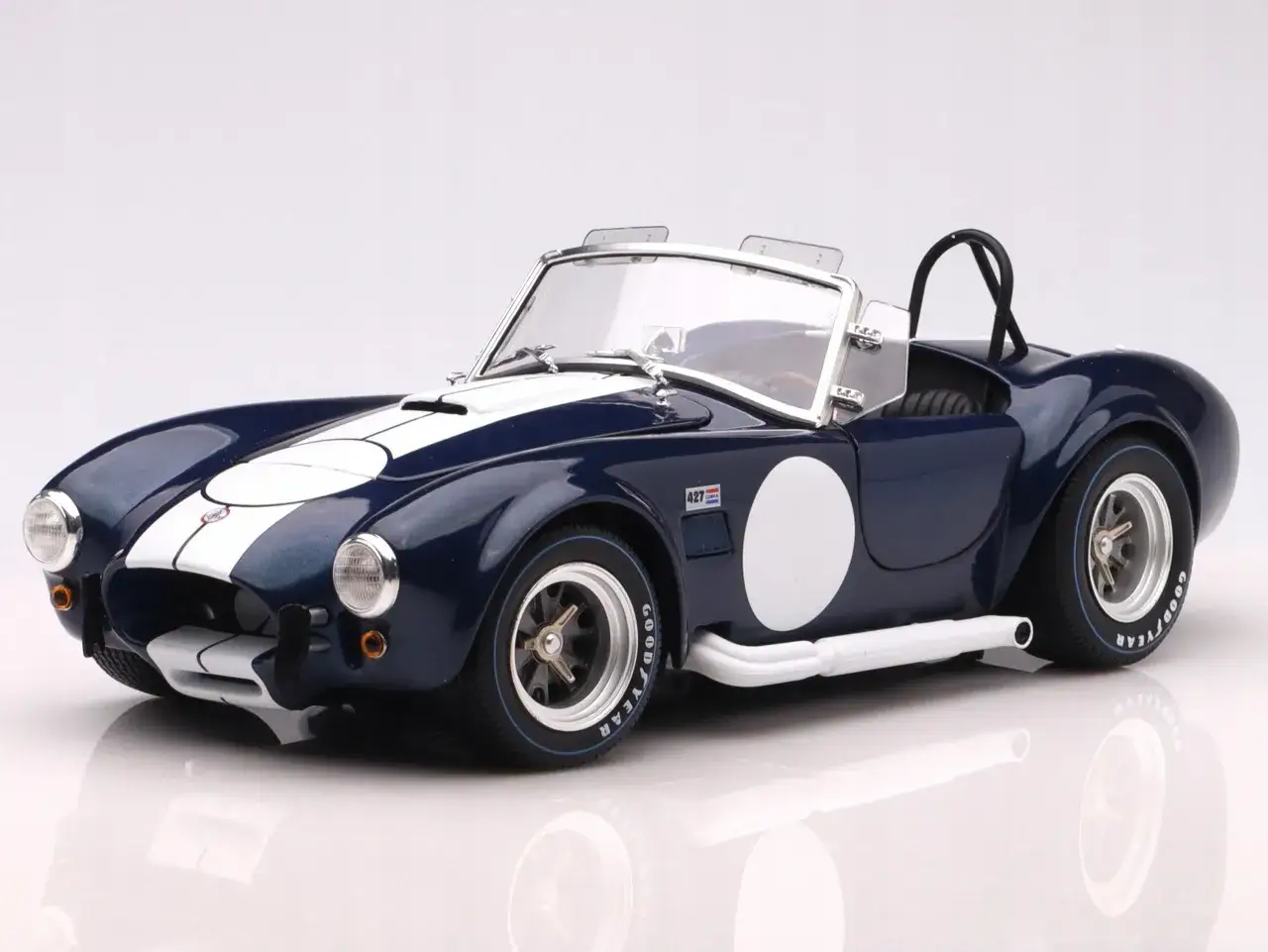 Granatowy Shelby Cobra z białymi pasami i okrągłymi emblematami. Marzenie o tym klasyku, jego shelby cobra cena, jest blisko.