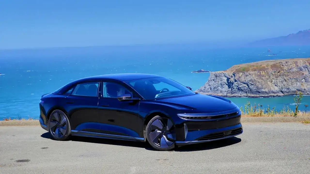 Lśniący, granatowy Lucid Air Grand Touring na tle błękitnego oceanu i skalistego wybrzeża.