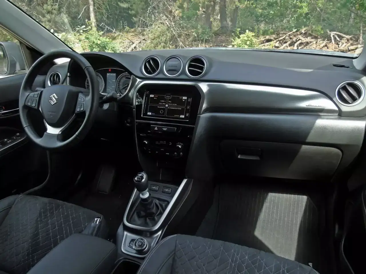 Wnętrze Suzuki Vitara. Kierownica, deska rozdzielcza z ekranem multimedialnym i dźwignia zmiany biegów. Sprawdź suzuki vitara cena!