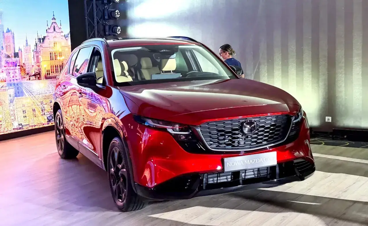 Nowa Mazda CX-5, lśniąca czerwień, prezentowana na tle miejskiego krajobrazu. Ta hybryda zachwyca designem.