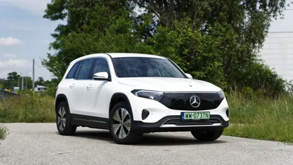 Biały Mercedes EQB na tle zieleni i nieba. Elektryczny SUV z charakterystycznym grillem i nowoczesnymi światłami.
